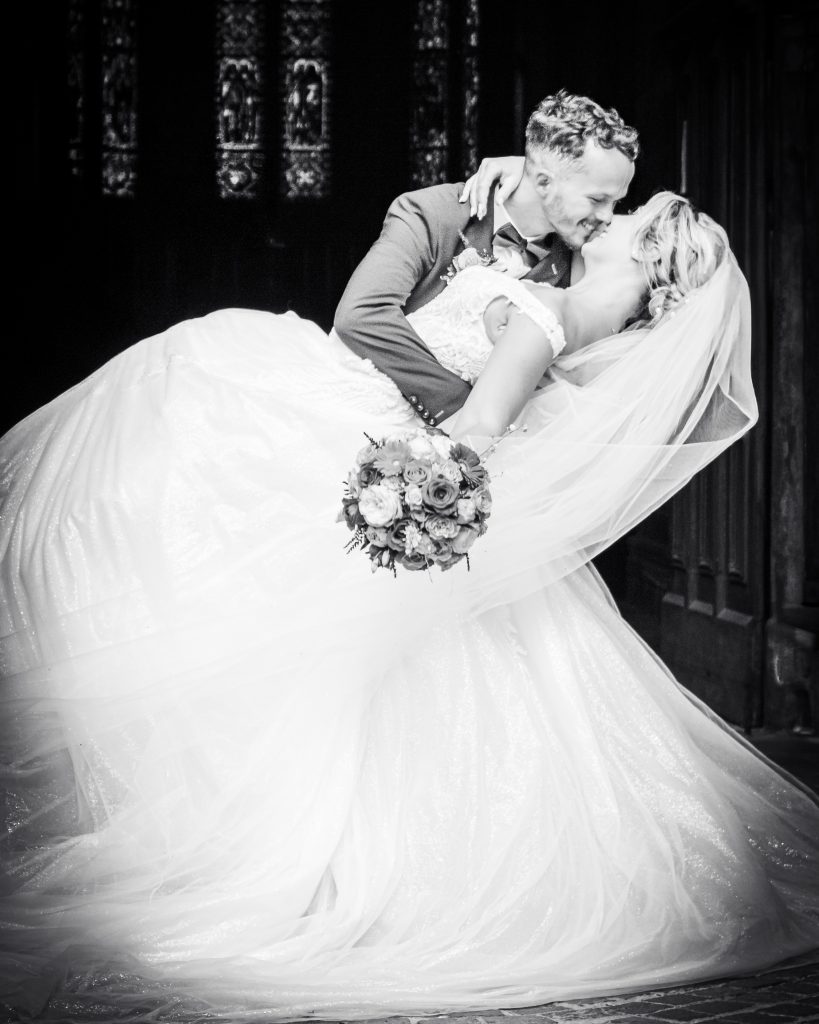 Couple de mariés s’embrassant lors d’une pose romantique, la mariée tenue dans les bras du marié.