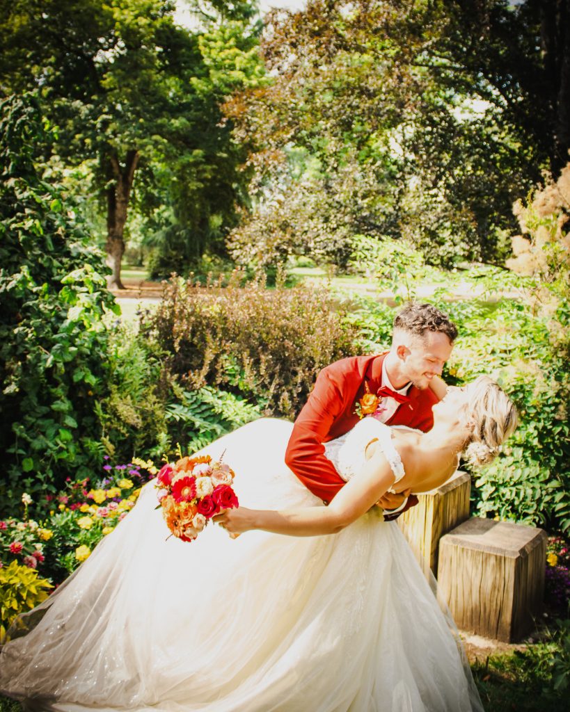 Mariés dans une pose romantique dans un jardin fleuri, le marié tenant la mariée dans ses bras.