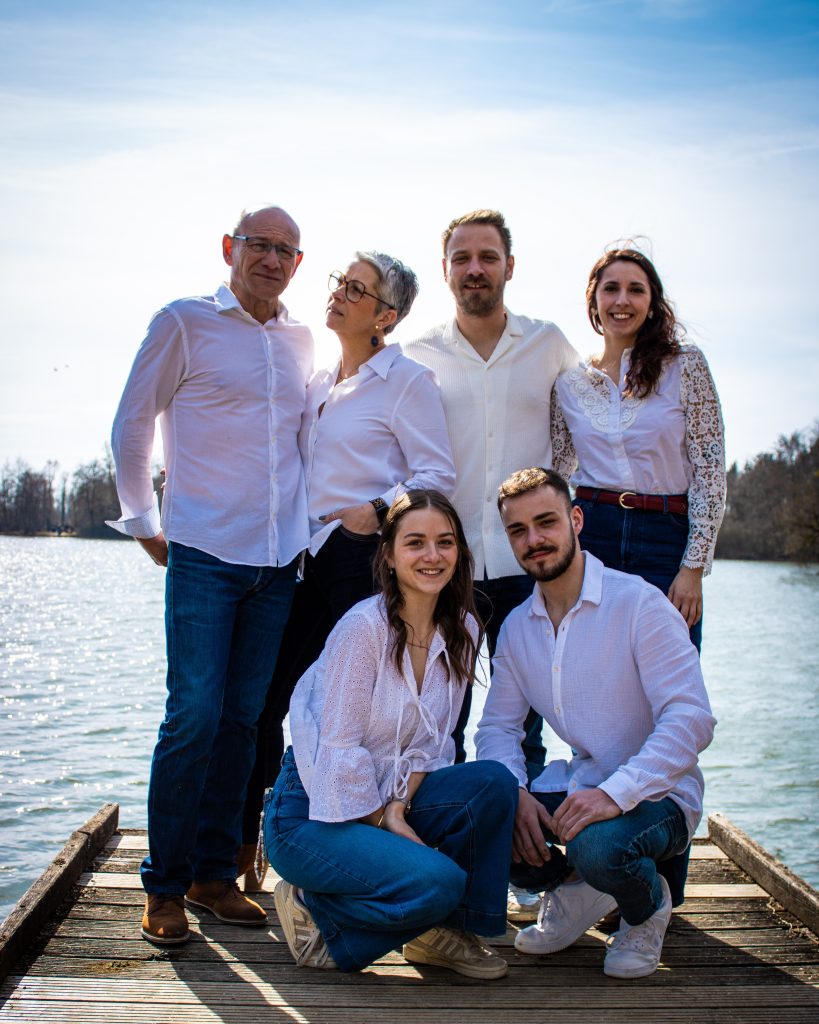 Photo de famille posant ensemble en extérieur sur un ponton au bord de l’eau.