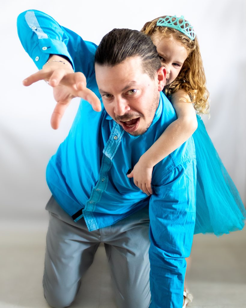 Parent jouant avec son enfant lors d’une séance photo en studio, dans une pose amusante et dynamique.