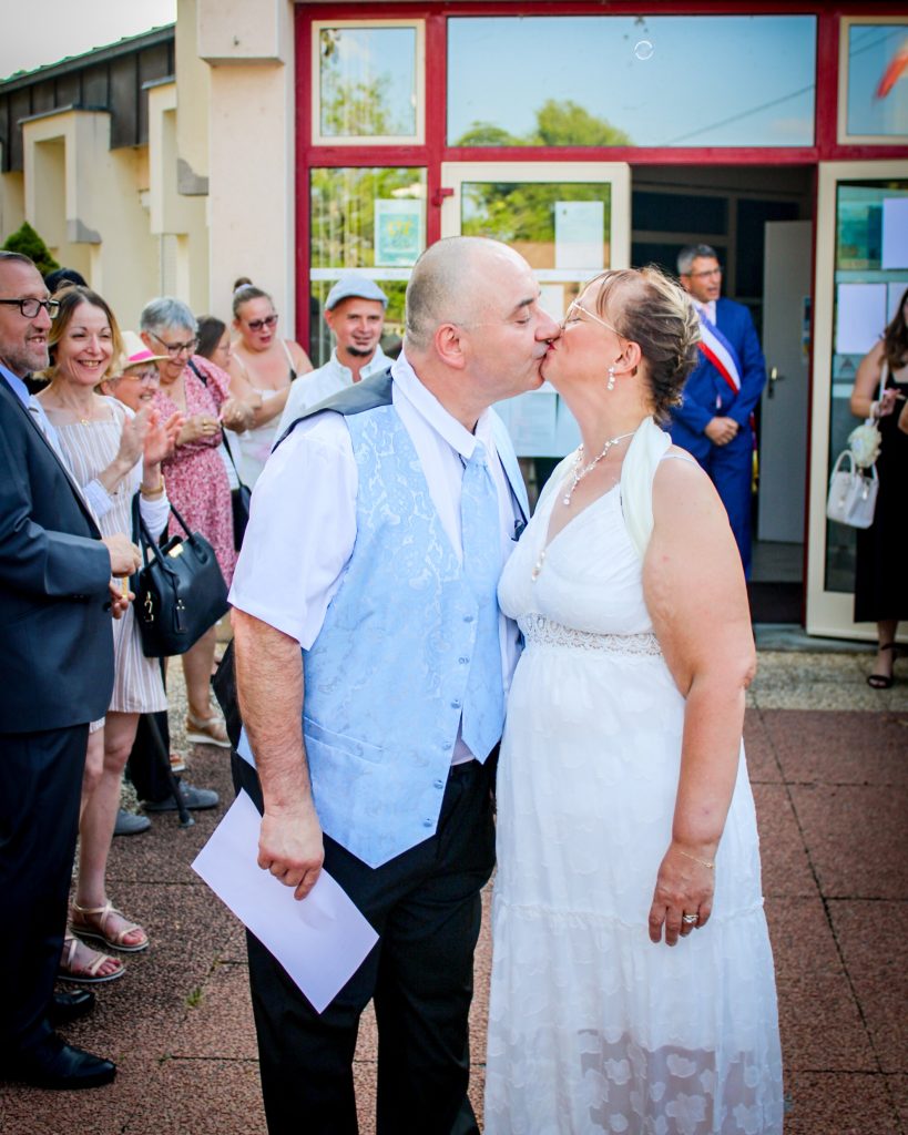 Couple s’embrassant à la sortie de la mairie, entouré de leurs proches.