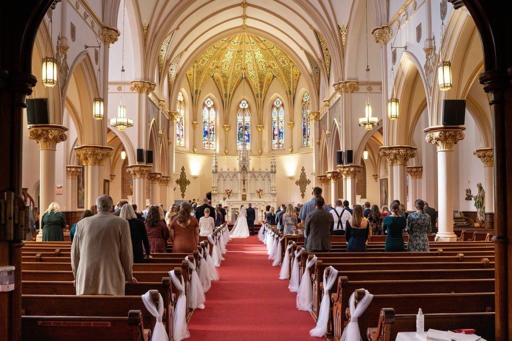 Cérémonie de mariage dans une église décorée, avec les invités assis et les mariés avançant dans l’allée centrale.