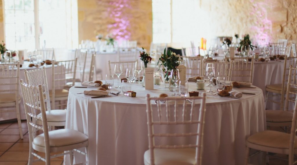 Salle de réception décorée pour un mariage, avec tables rondes élégamment dressées.